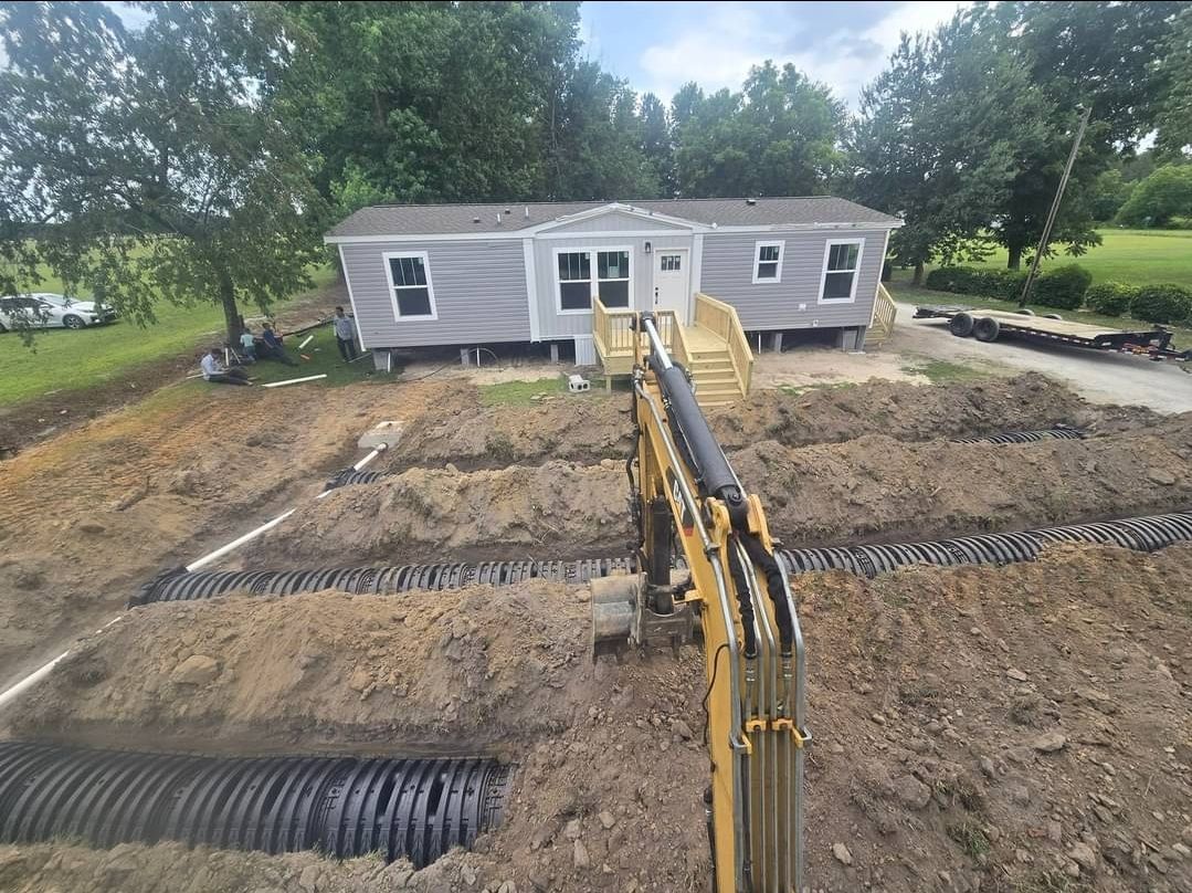 A yellow excavator is digging a hole in front of a mobile home.