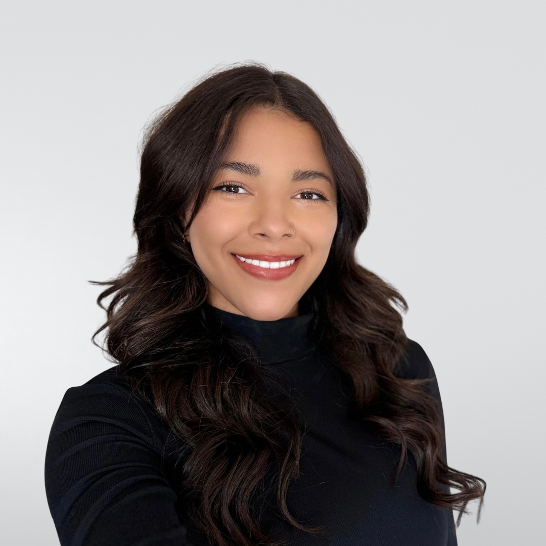 Woman with long, wavy dark hair smiles at the camera, wearing a black turtleneck.