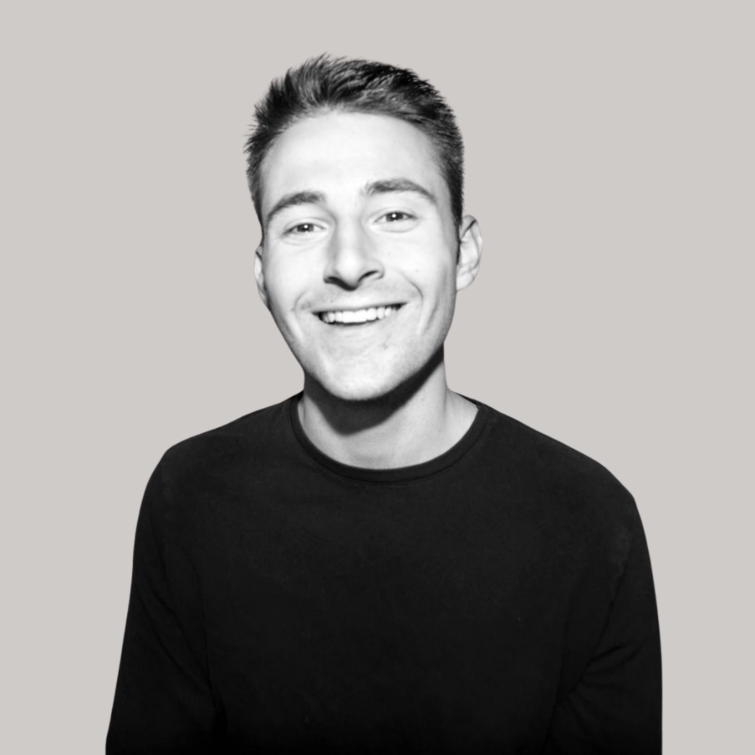 A young man in a black shirt is smiling in a black and white photo.