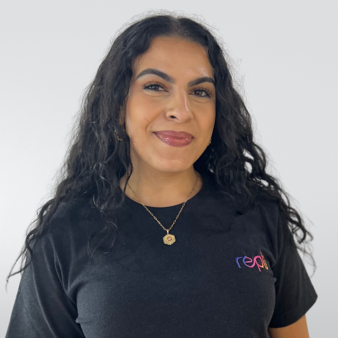 A woman wearing a black t-shirt and a necklace is smiling for the camera.