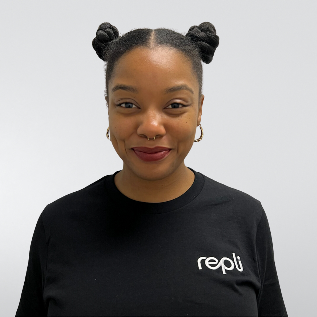 A woman wearing a black repli shirt smiles for the camera