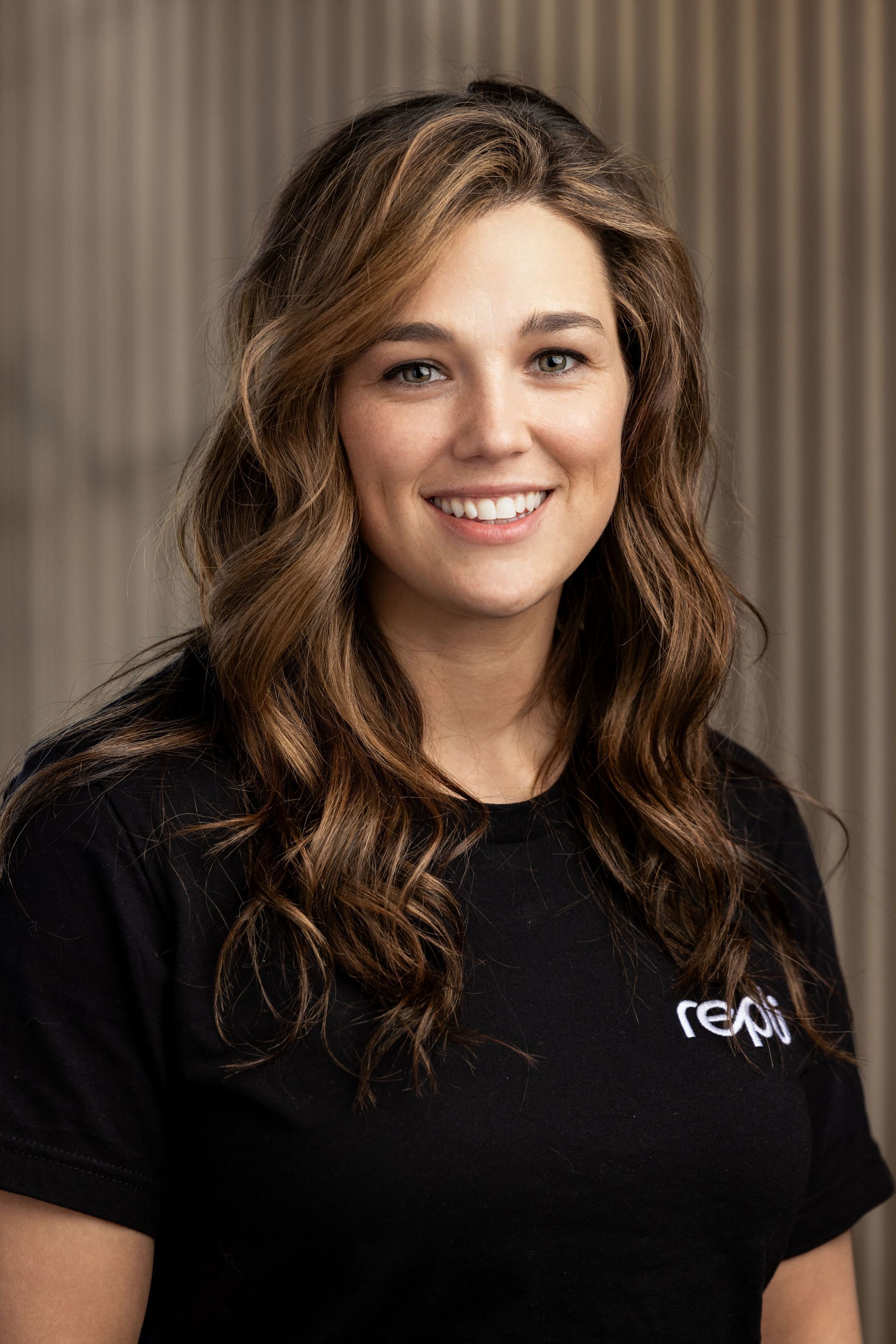 A woman with long blonde hair is smiling and wearing a black shirt.