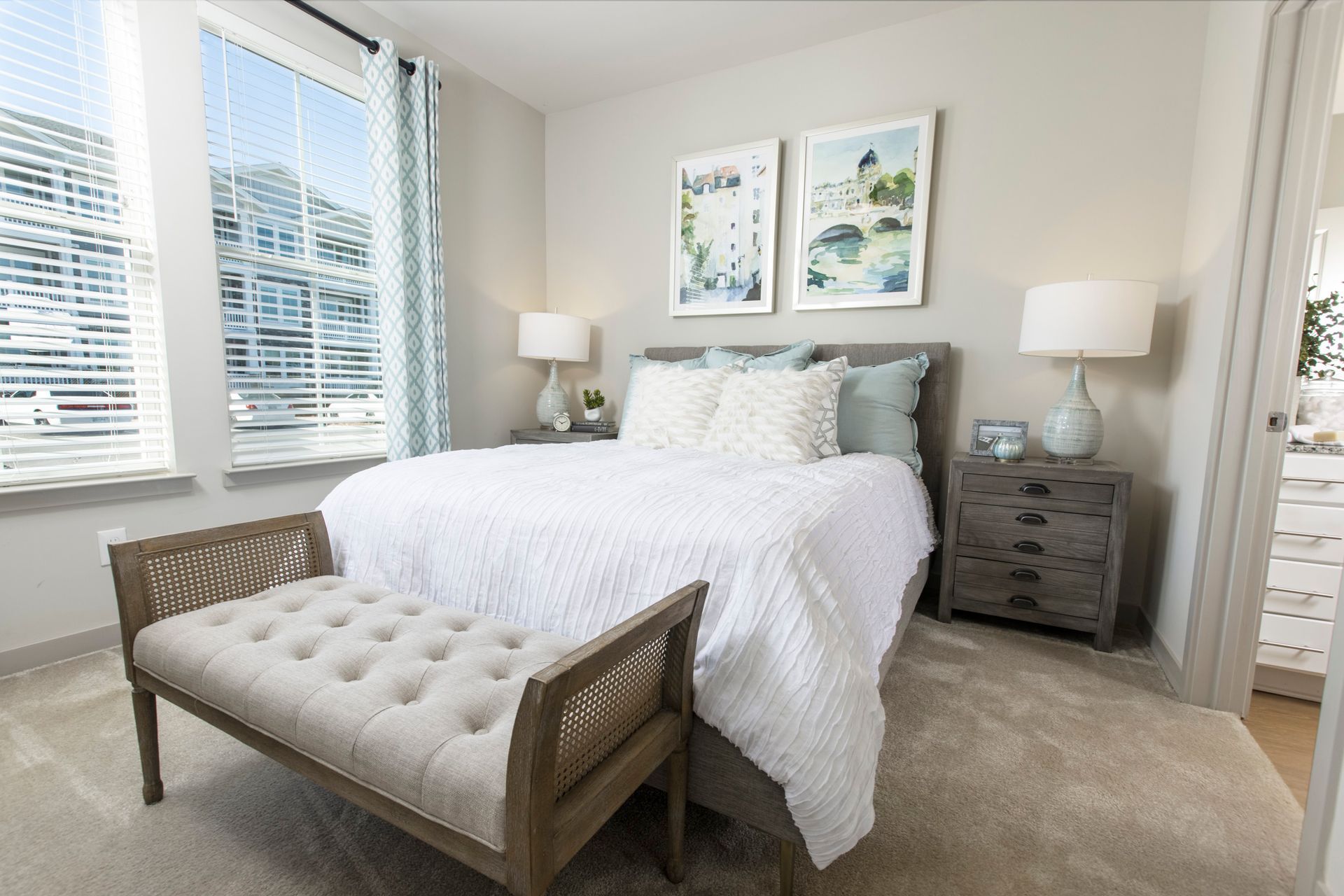 A bedroom with a bed , nightstand , lamps and a bench.