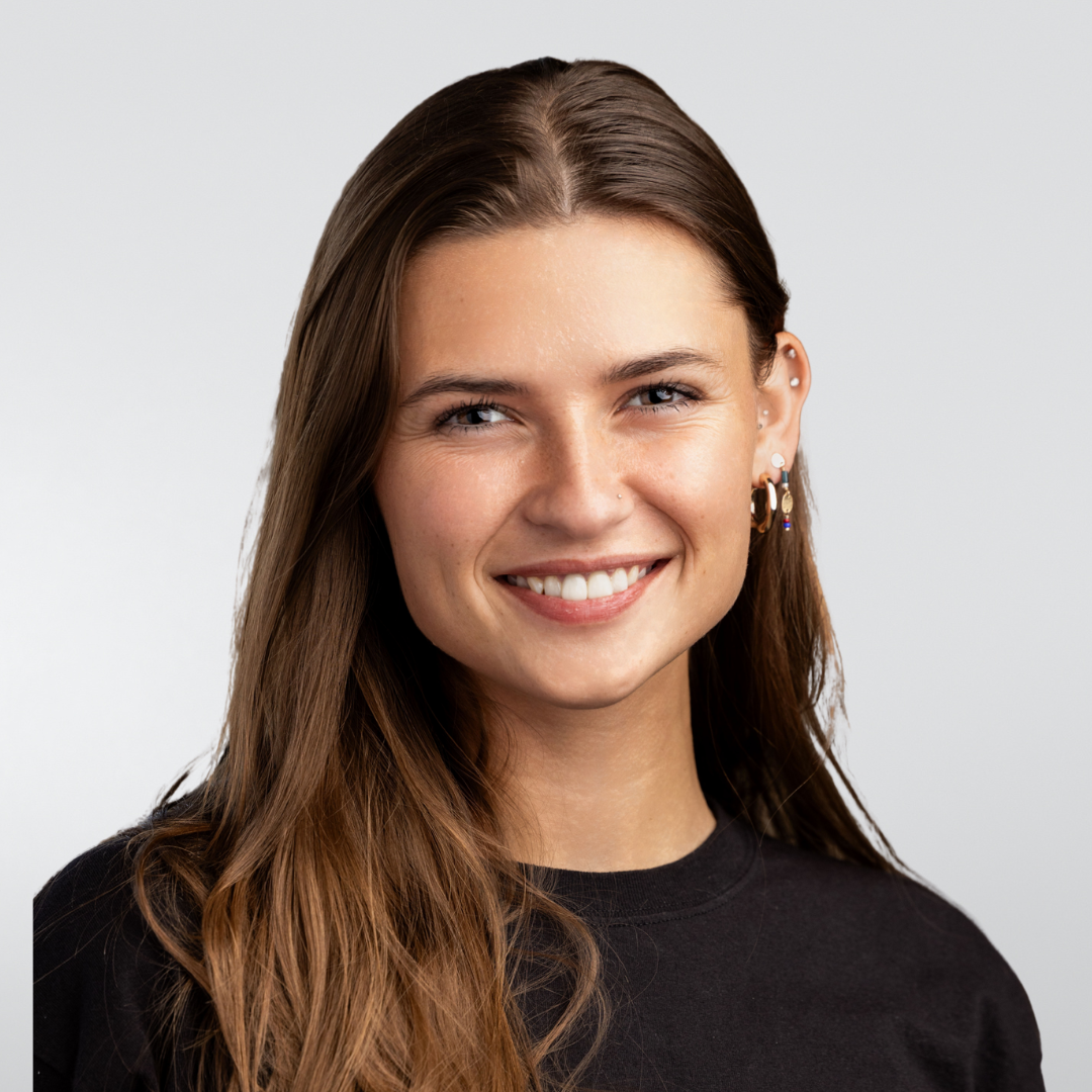 A woman wearing a black tank top and a necklace is smiling for the camera.