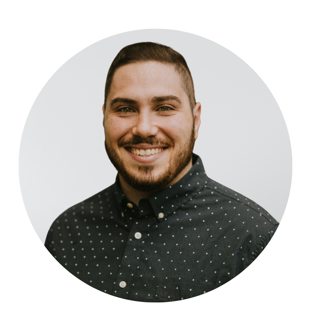 A man with a beard is wearing a black polka dot shirt and smiling.