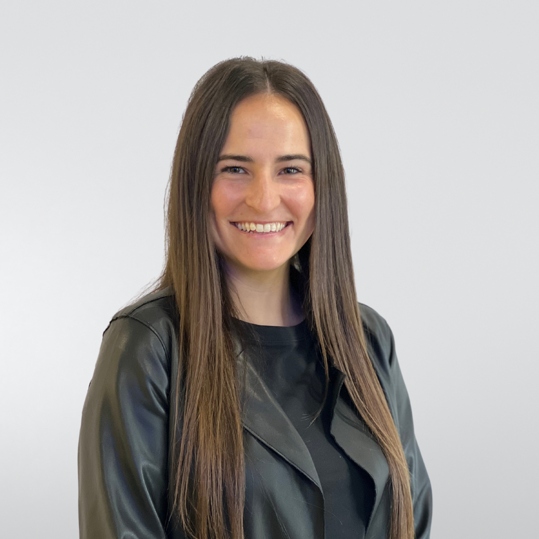 A woman with long hair is wearing a black leather jacket and smiling.