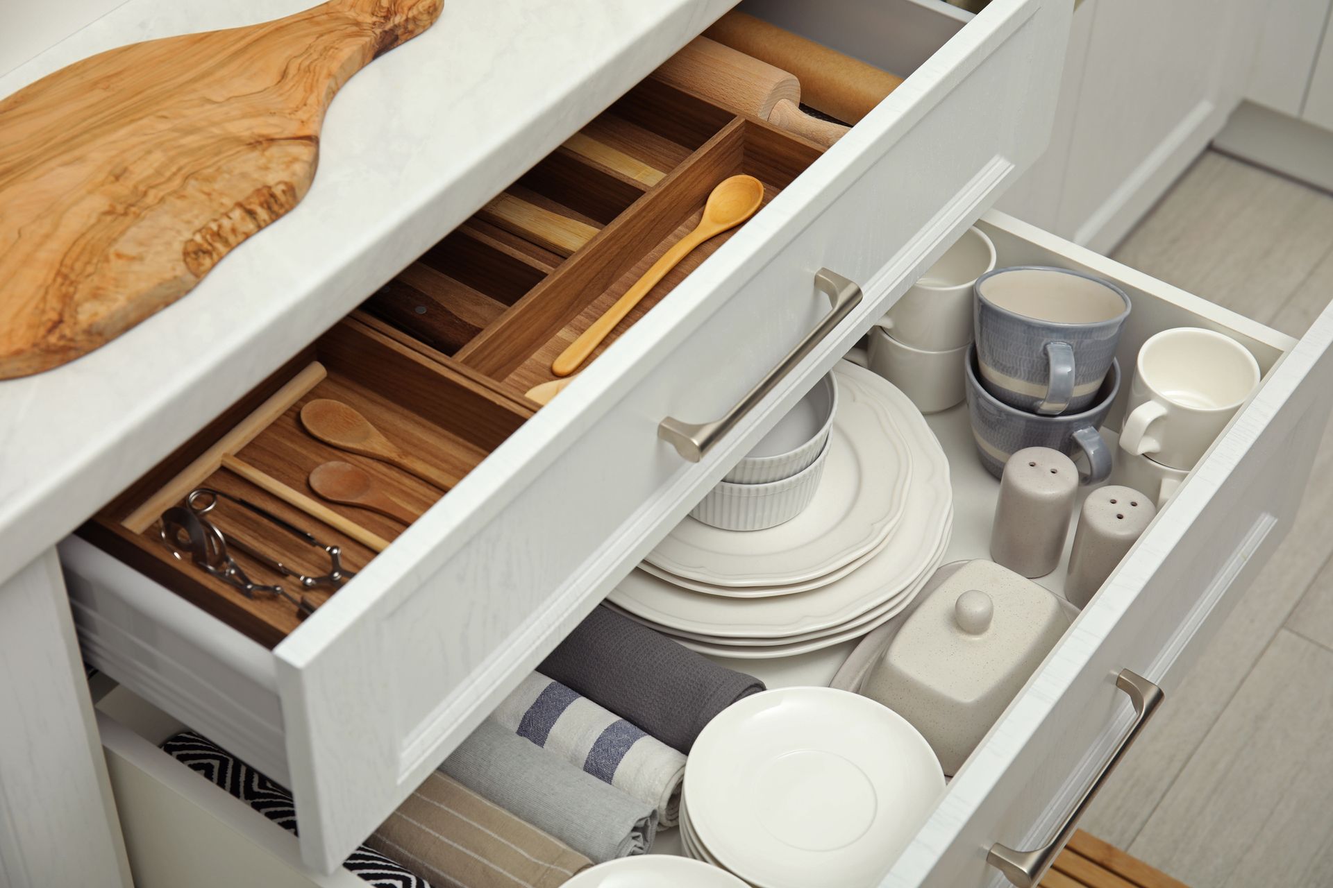 Open kitchen drawers filled with utensils, plates, and mugs.