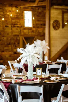 Elegant wedding table settings in a rustic barn, featuring white feather centerpieces on black tablecloths.