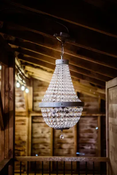 A teardrop-shaped crystal chandelier hangs from the wooden rafters of a rustic barn interior.