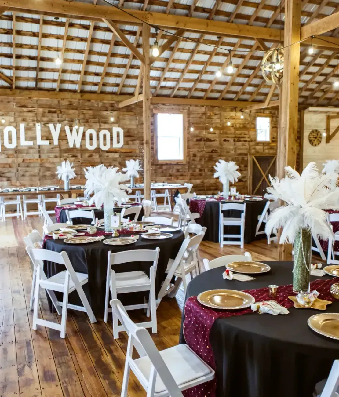 A rustic barn event space decorated for a Hollywood-themed event with round tables and white chairs.