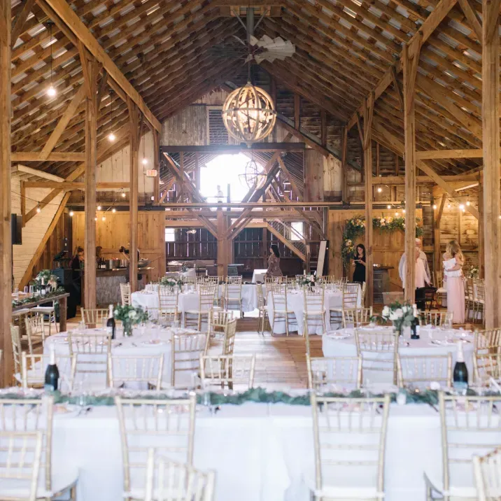 A rustic barn event space set for a wedding reception with round tables, white tablecloths, and a large spherical light.