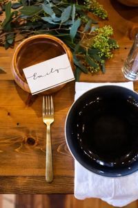 A gold fork, a dark bowl on a white napkin, and a name card for 