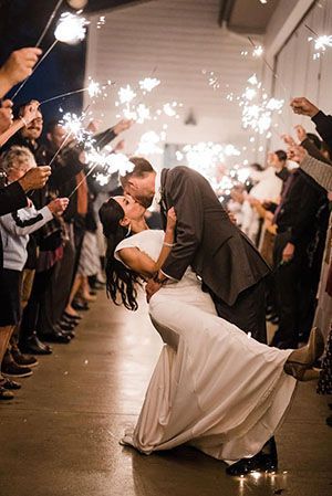 A couple kisses while dipping during a wedding sparkler exit, surrounded by guests holding glowing sparklers.