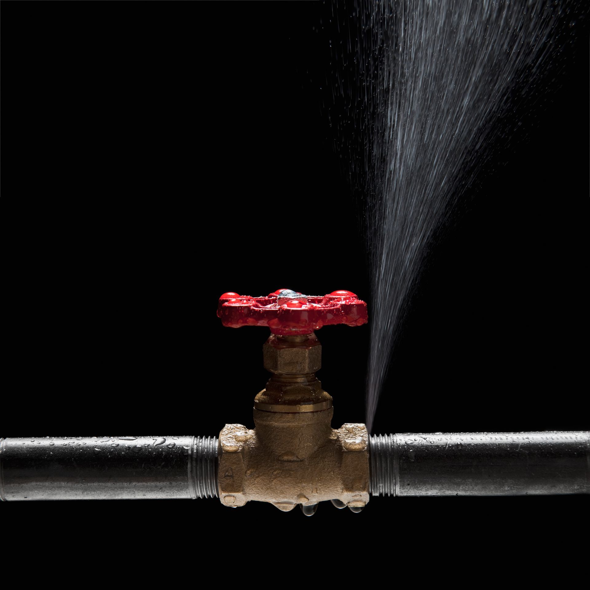 Water sprays from a cracked pipe near a red valve, showing a visible plumbing leak.