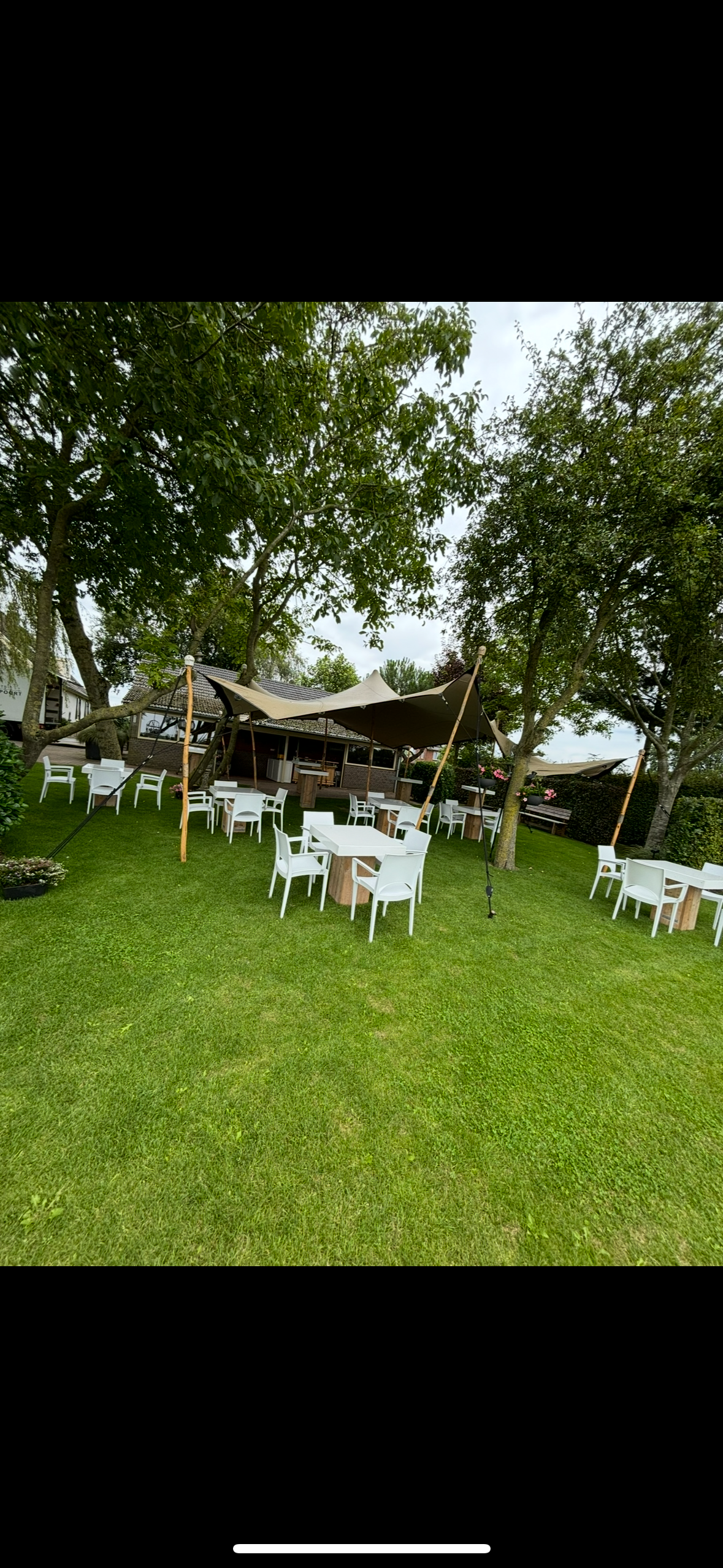 Een groep tafels en stoelen staat onder een tent in een grasveld.