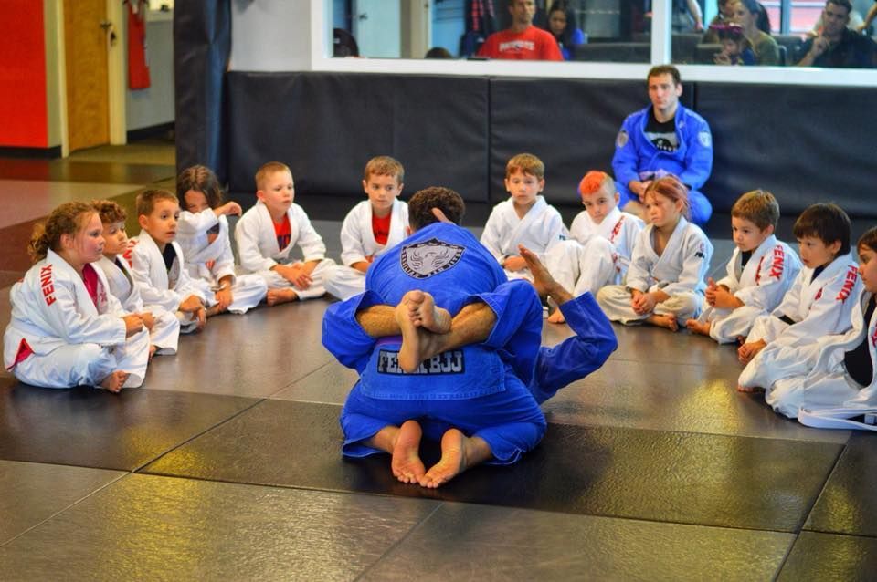 A group of children are sitting on the floor watching a Jiu Jitsu class