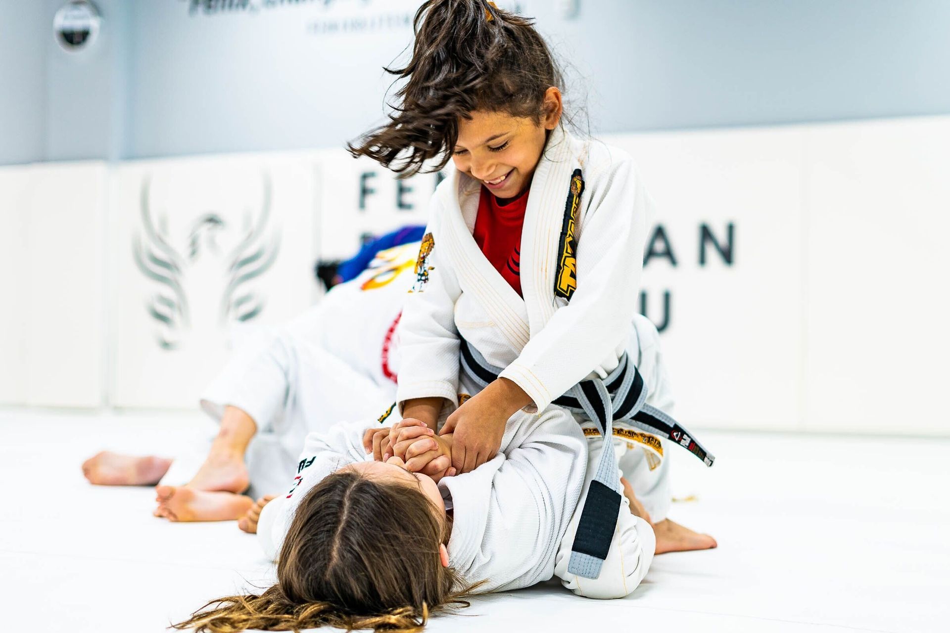 Two young girls are practicing jiu jitsu in a gym.