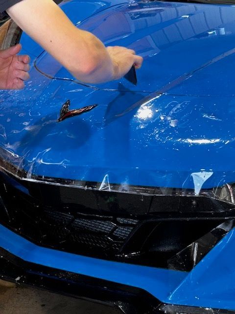 A person is wrapping the hood of a blue car