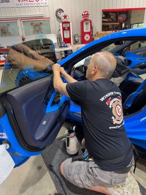 A man in a black shirt is working on a blue car.