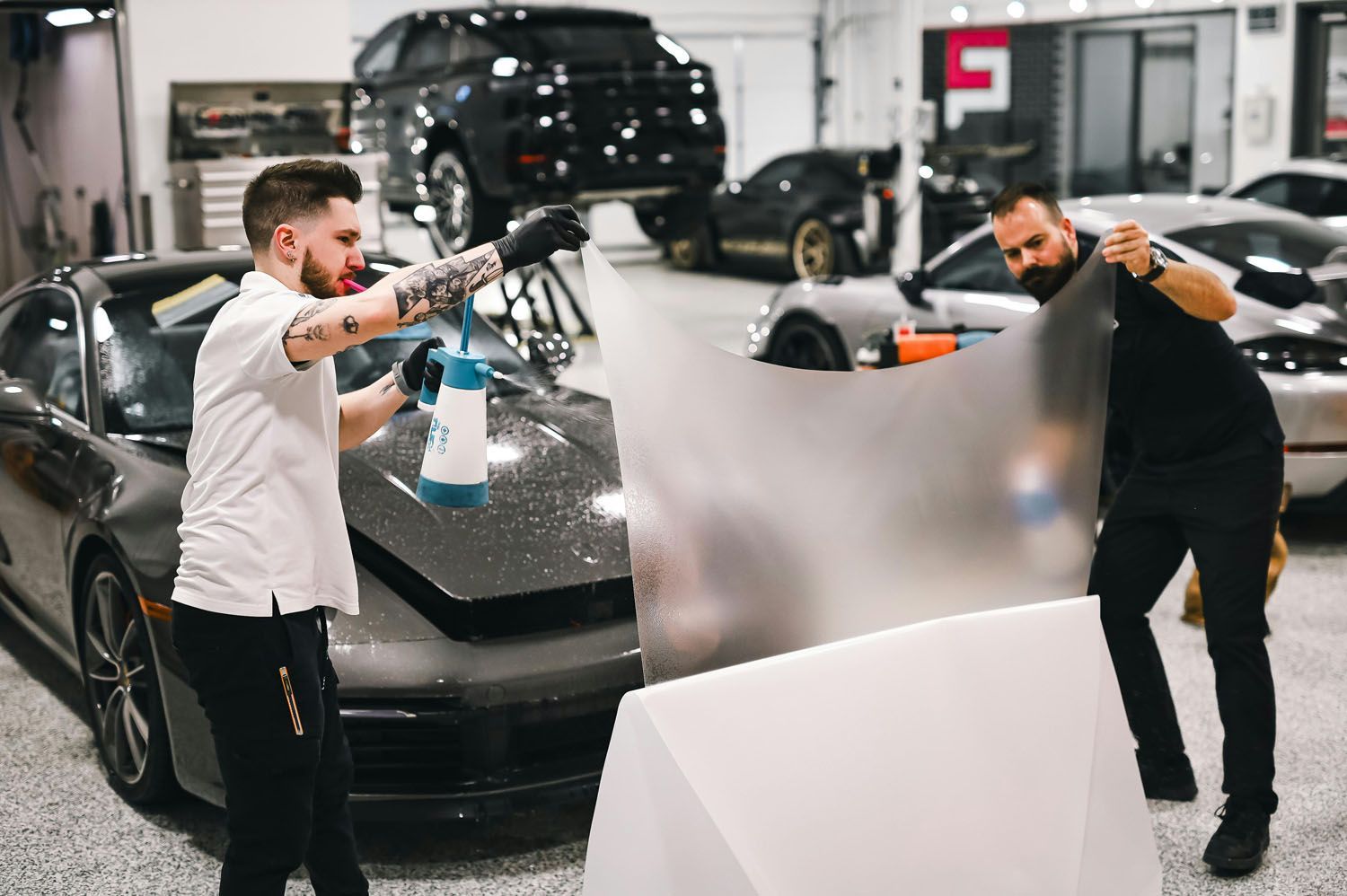 Two men are wrapping a car in a garage.