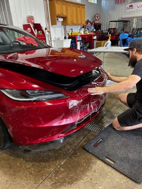 A man is kneeling down in front of a red tesla model 3.