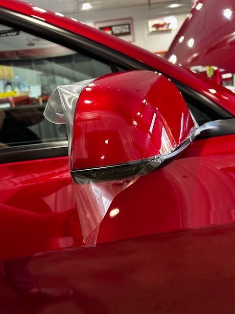 A red car with the side mirror wrapped in plastic