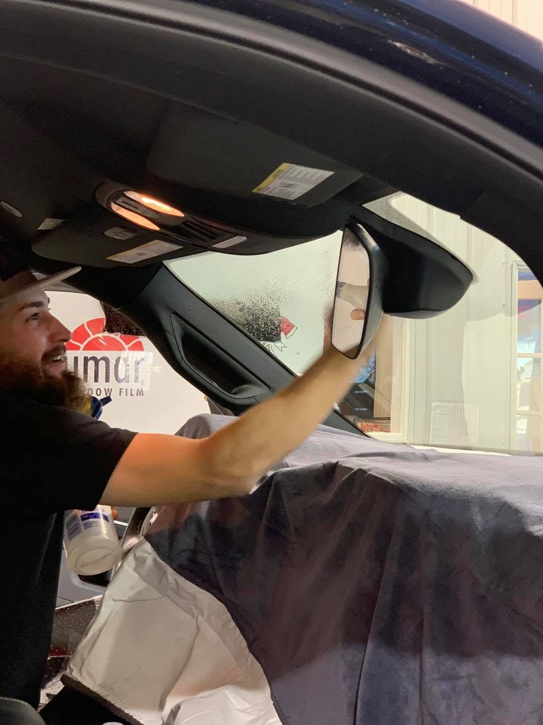 A man is sitting in a car looking at his rear view mirror