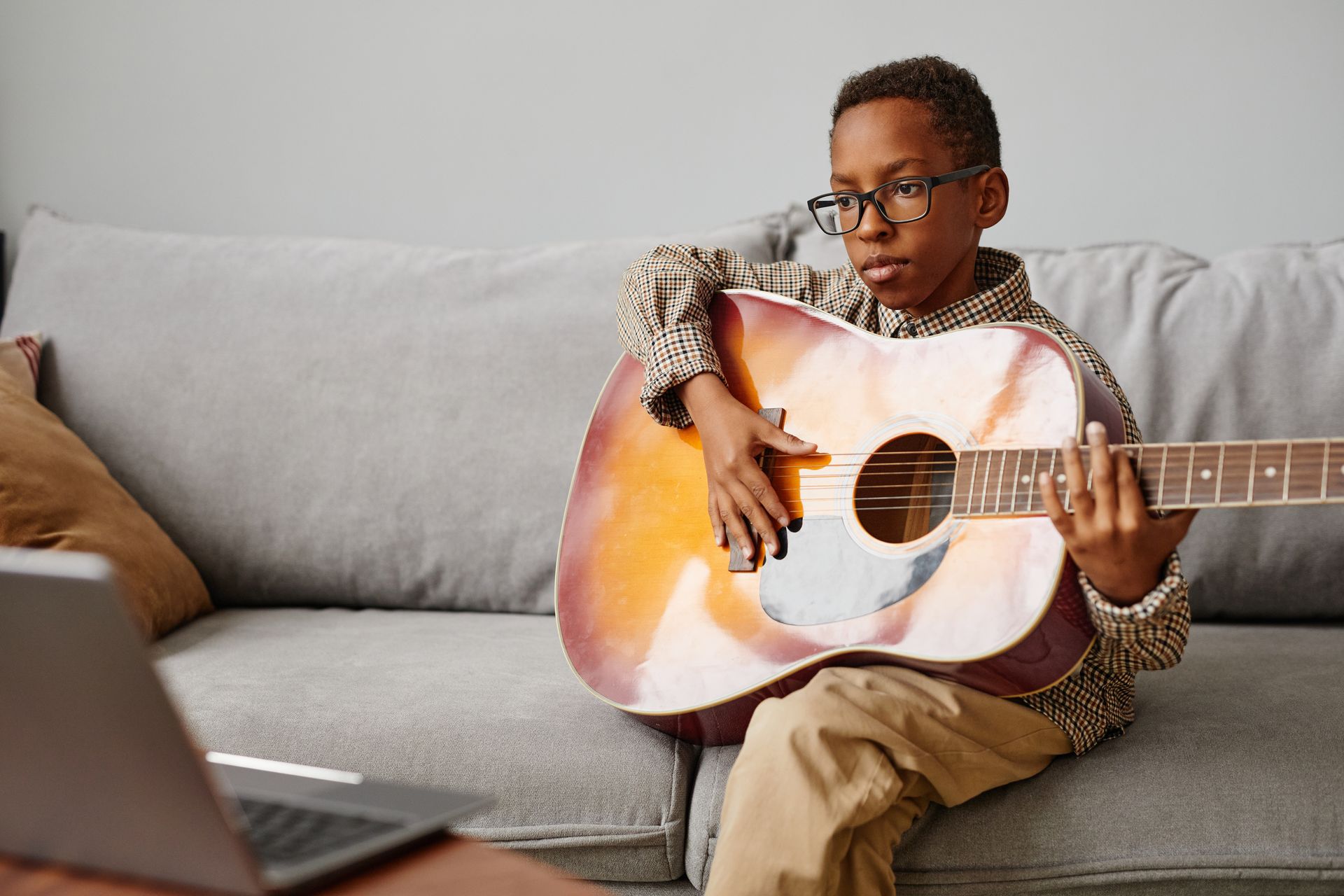 A young boy is sitting on a couch playing an acoustic guitar.