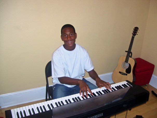 A young boy is sitting at a keyboard with a guitar in the background