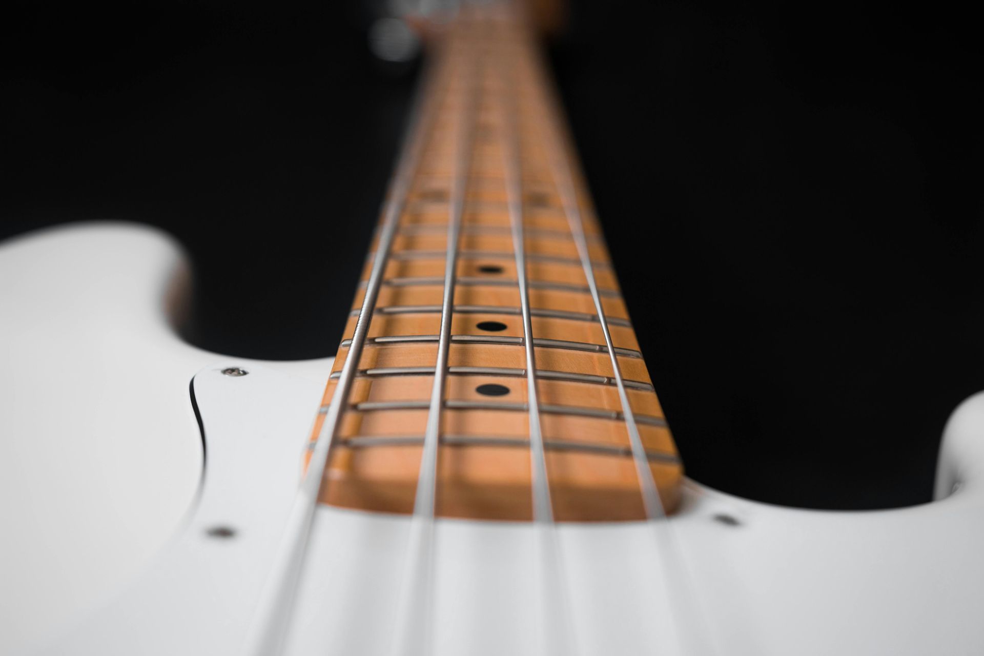 A close up of a white electric guitar on a black background.