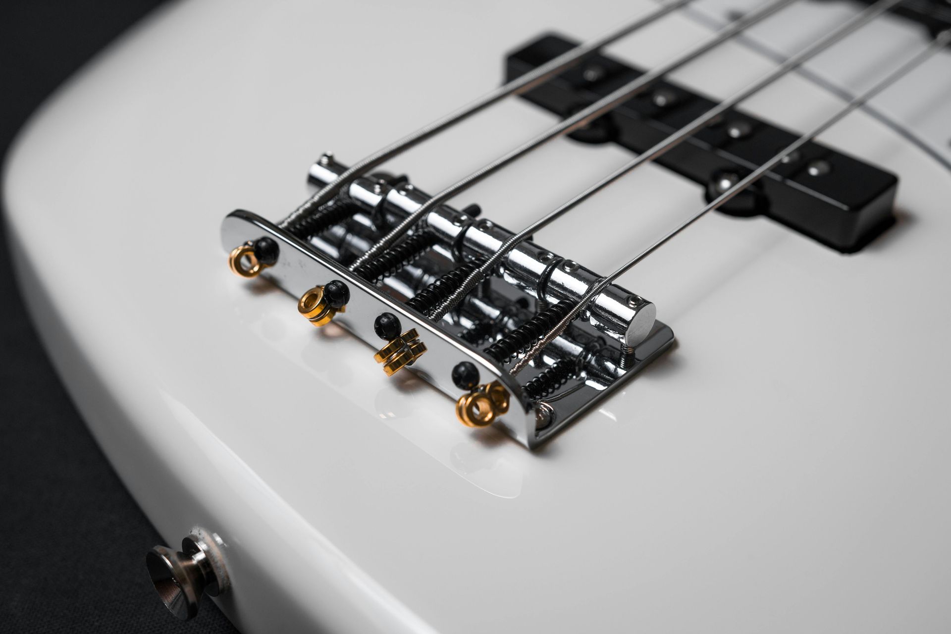 A close up of the bridge of a white bass guitar.