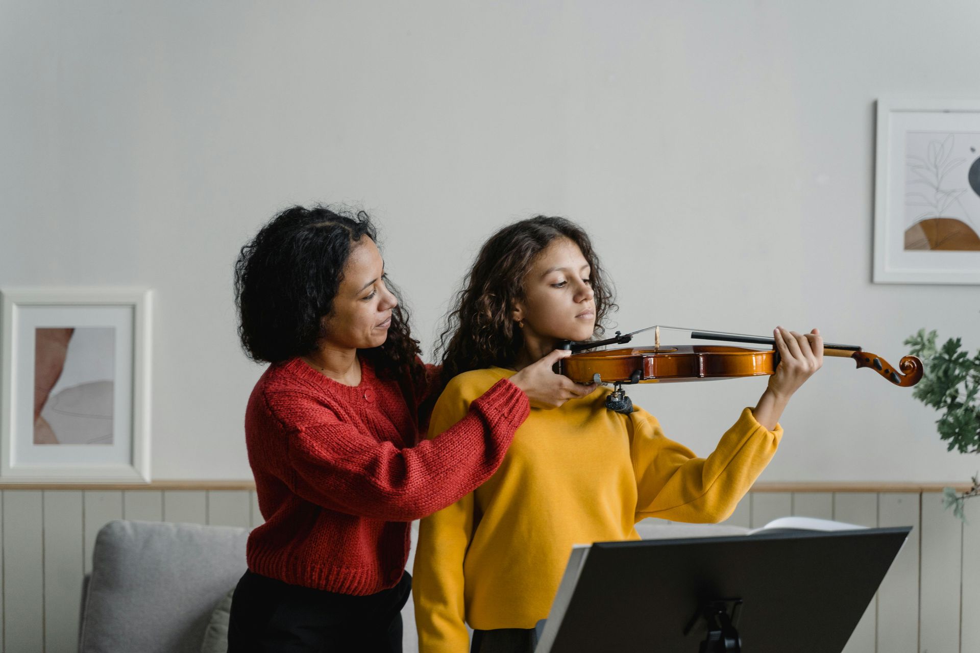 A woman is teaching a young girl how to play a violin.