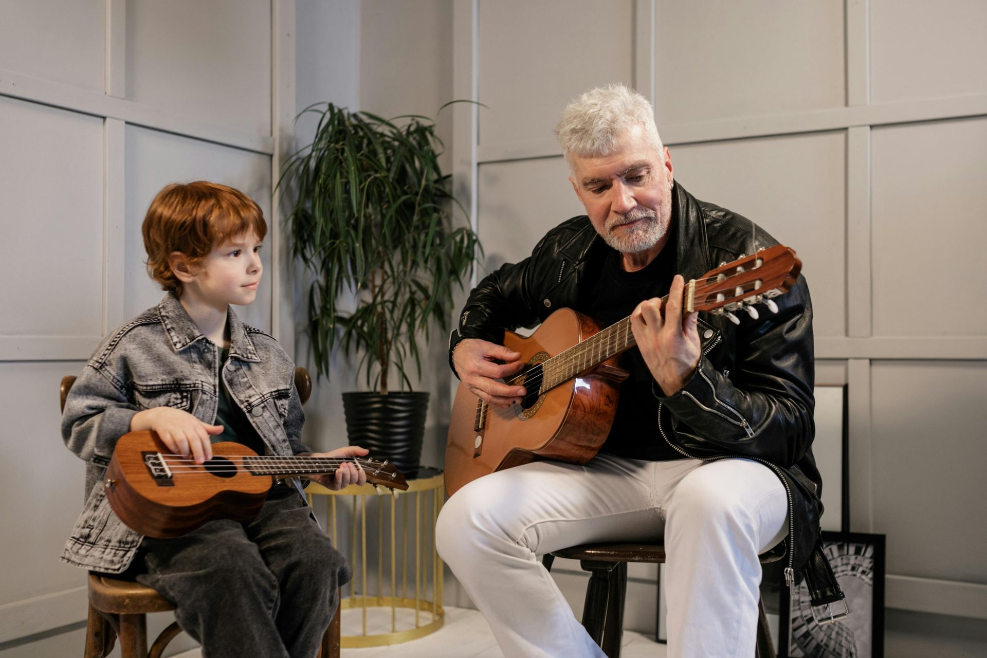 A man is teaching a young boy how to play a guitar.