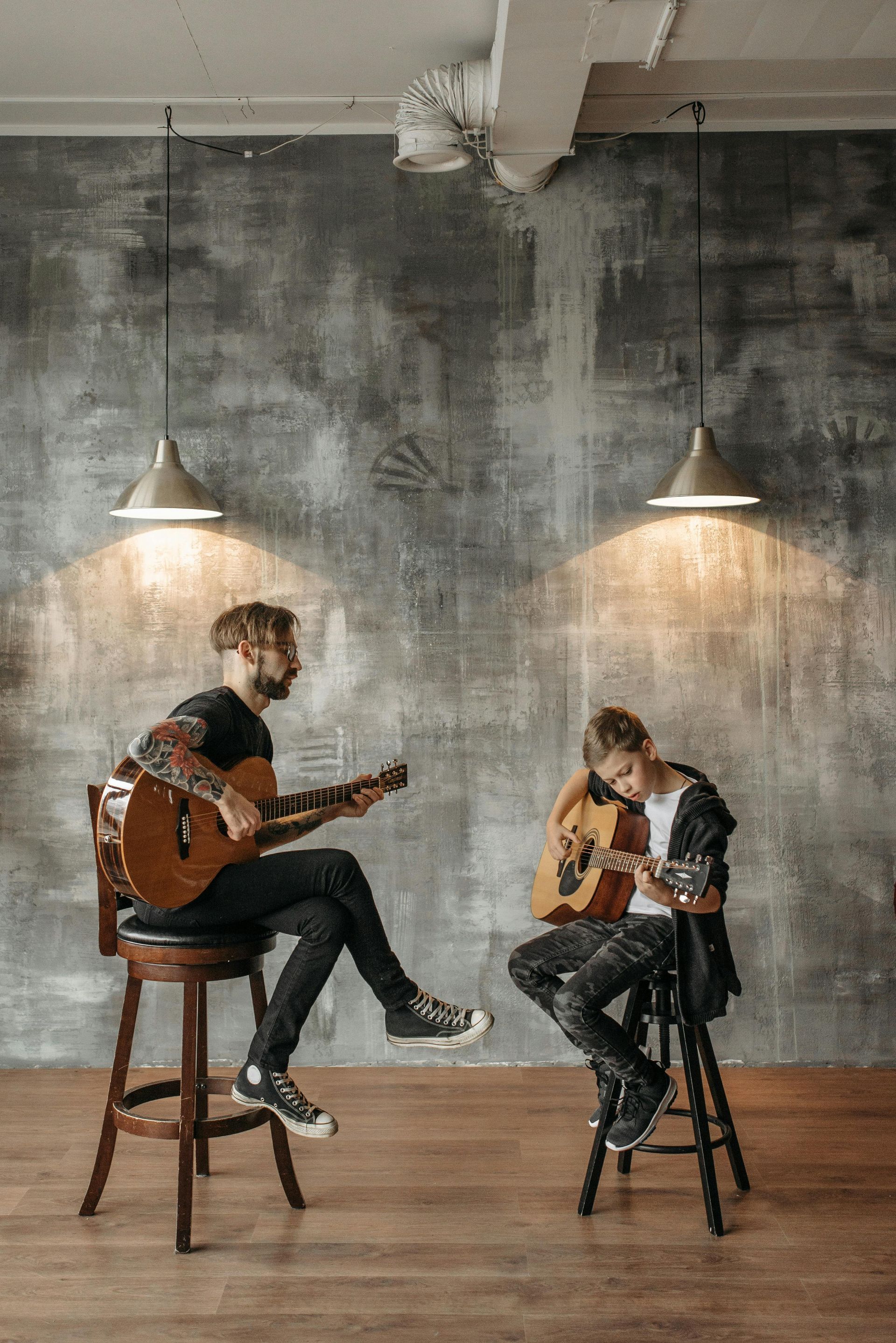 Two men are sitting on stools playing guitars in a room.