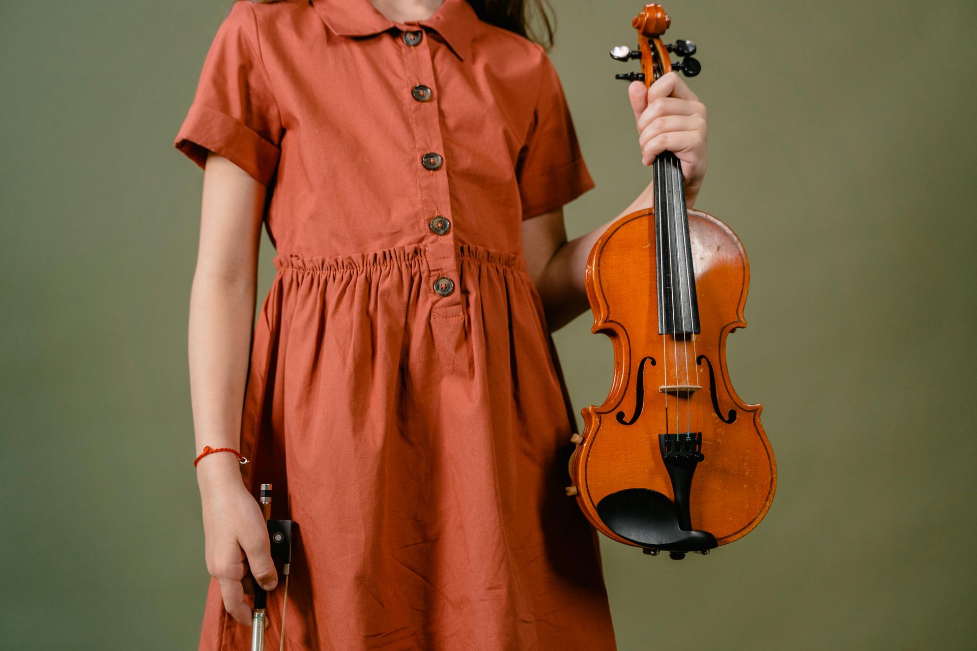 A young girl in a red dress is holding a violin.