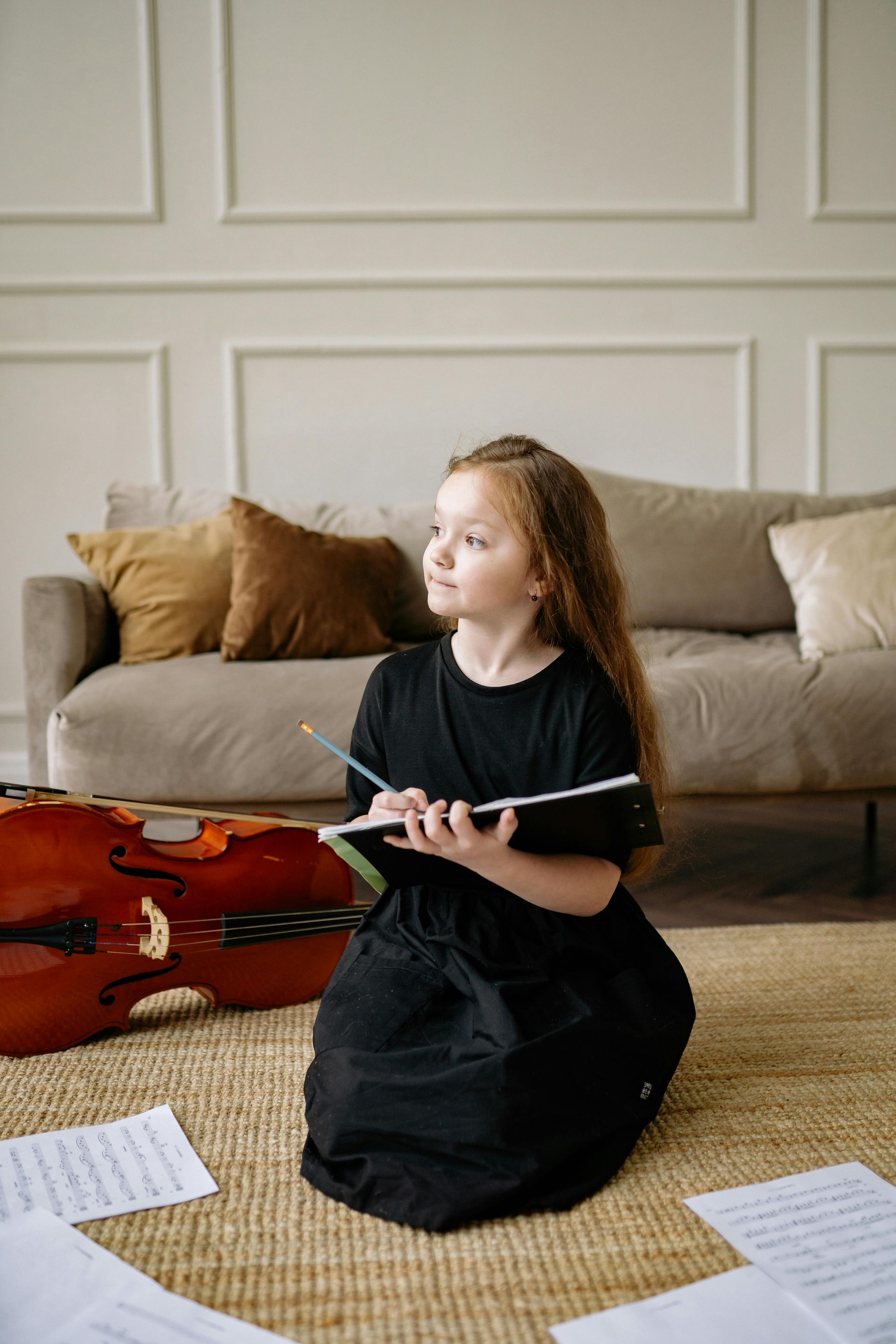 A little girl is sitting on the floor playing a violin.