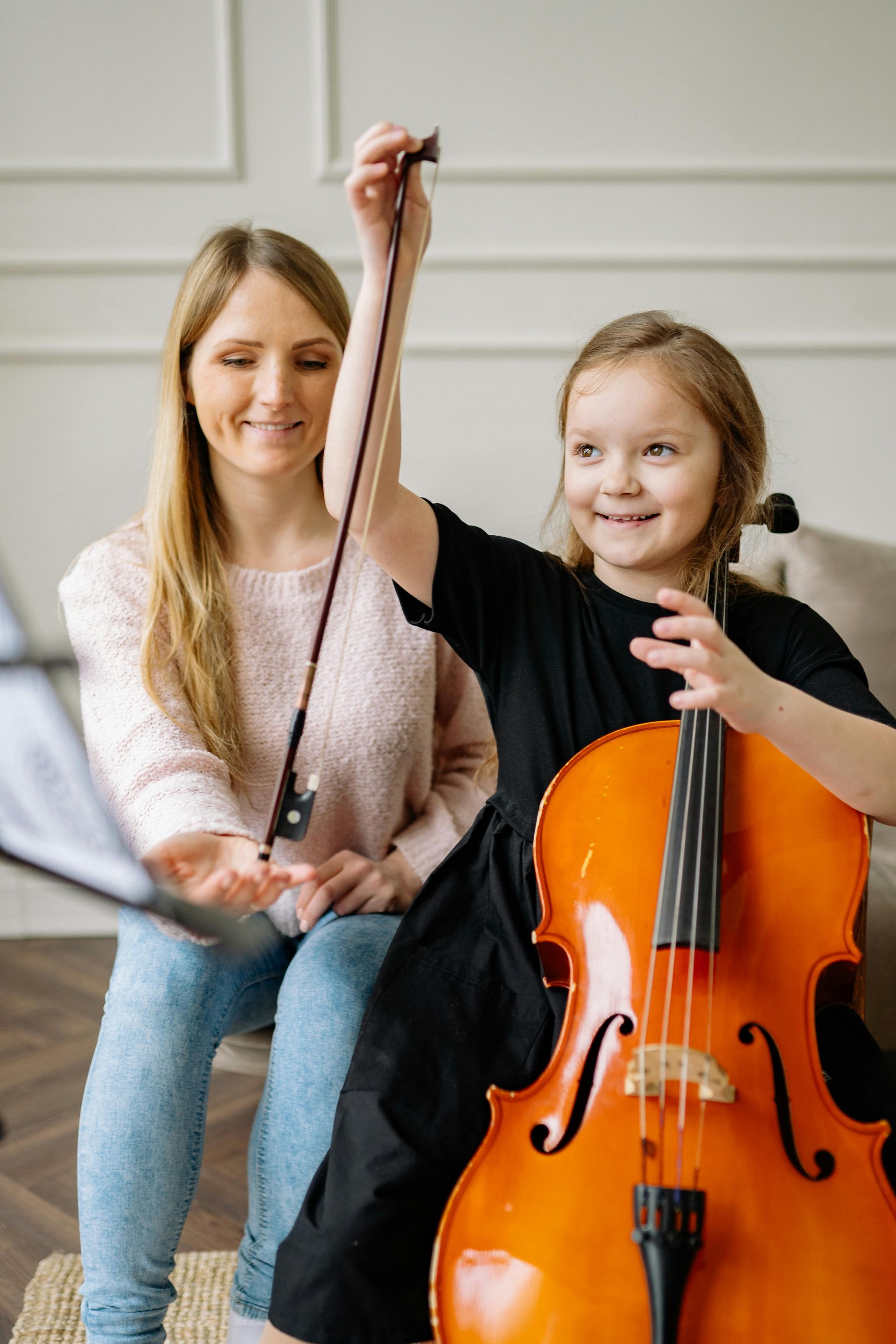 A woman is teaching a little girl how to play a cello.