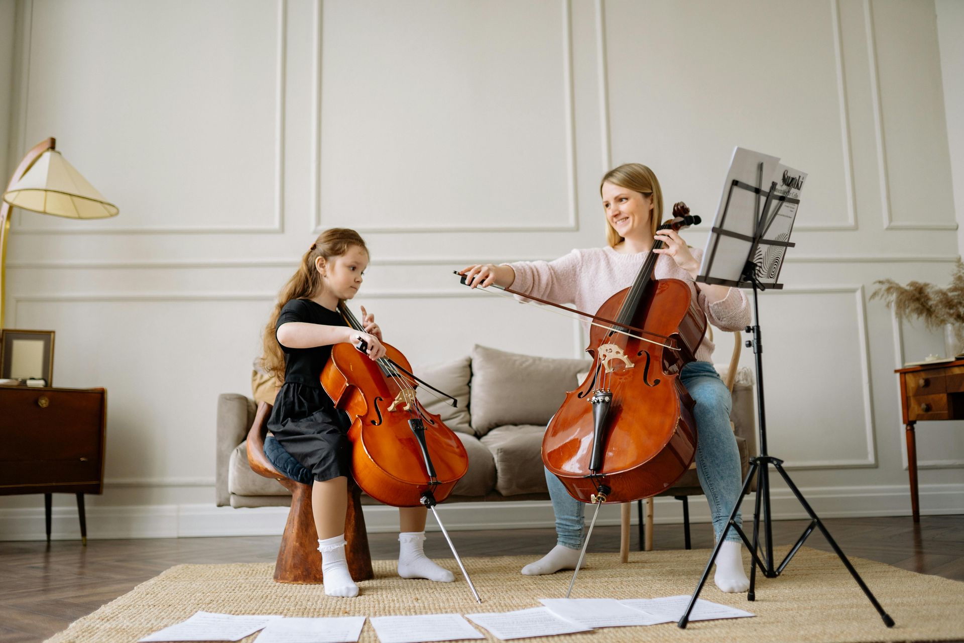 A woman and a girl are playing cello in a living room.