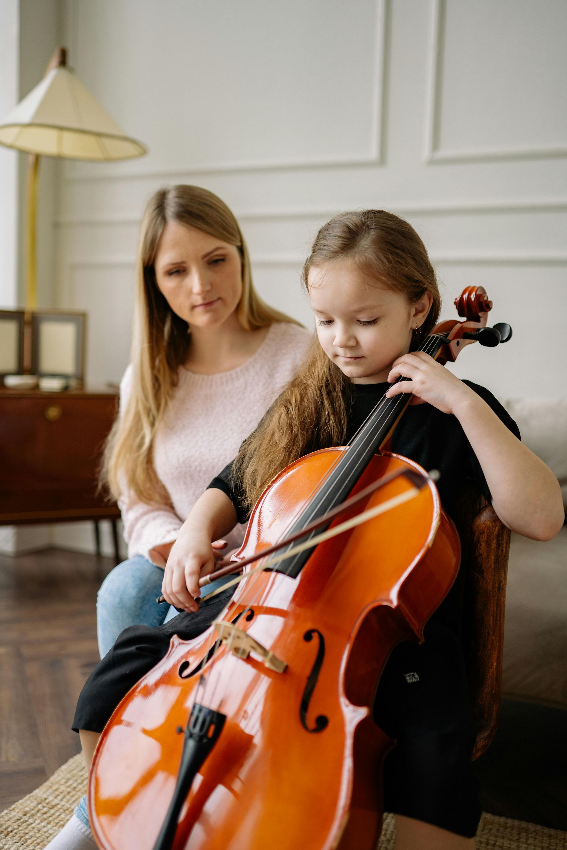 A woman is teaching a little girl how to play a cello.