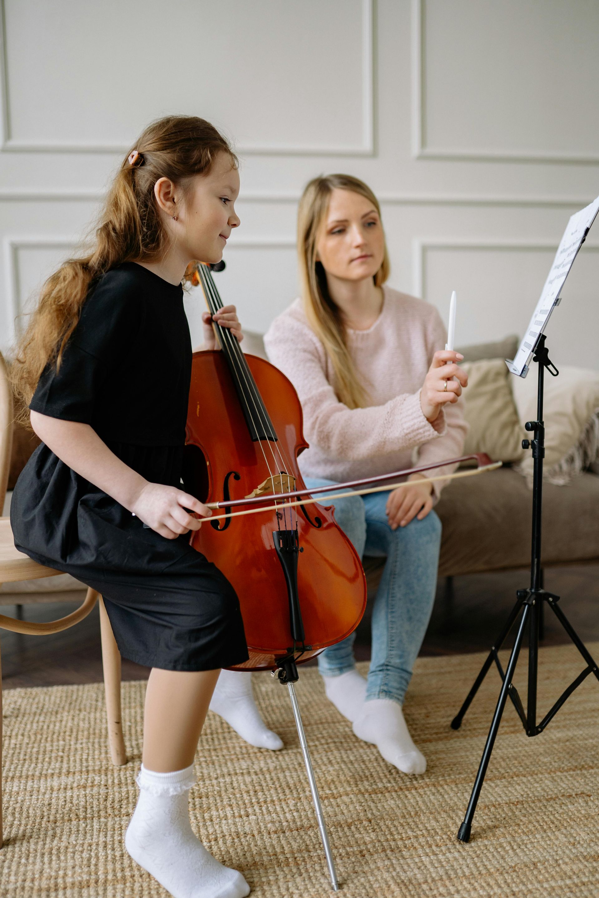 A woman is teaching a young girl how to play a cello.