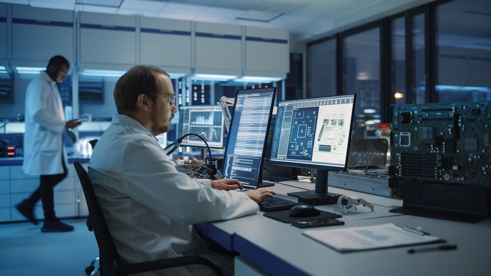Scientists working at computer stations in a modern lab control room, with monitors displaying data.
