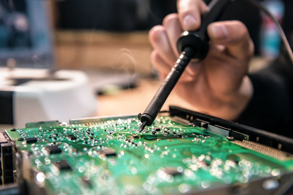 A person soldering an electronic circuit board with a soldering iron.