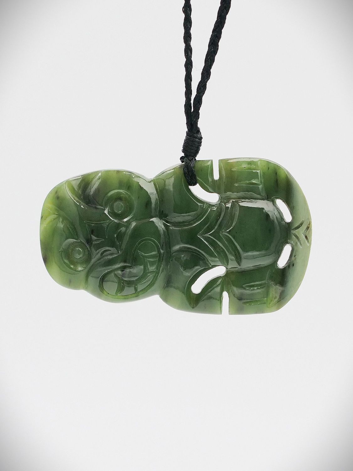 A pounamu hei tiki sculpture sitting against a black background
