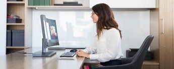 Woman in a white shirt and glasses on a video call at a desk.