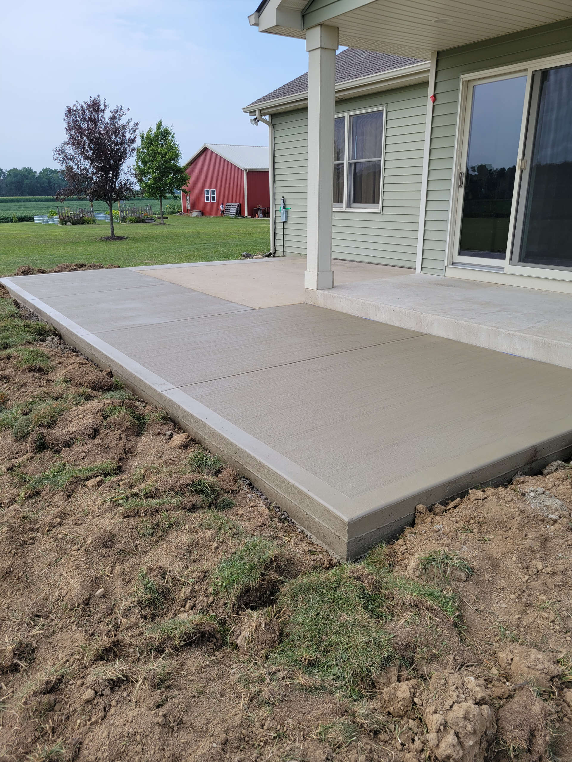 A concrete patio in front of a house with a red barn in the background