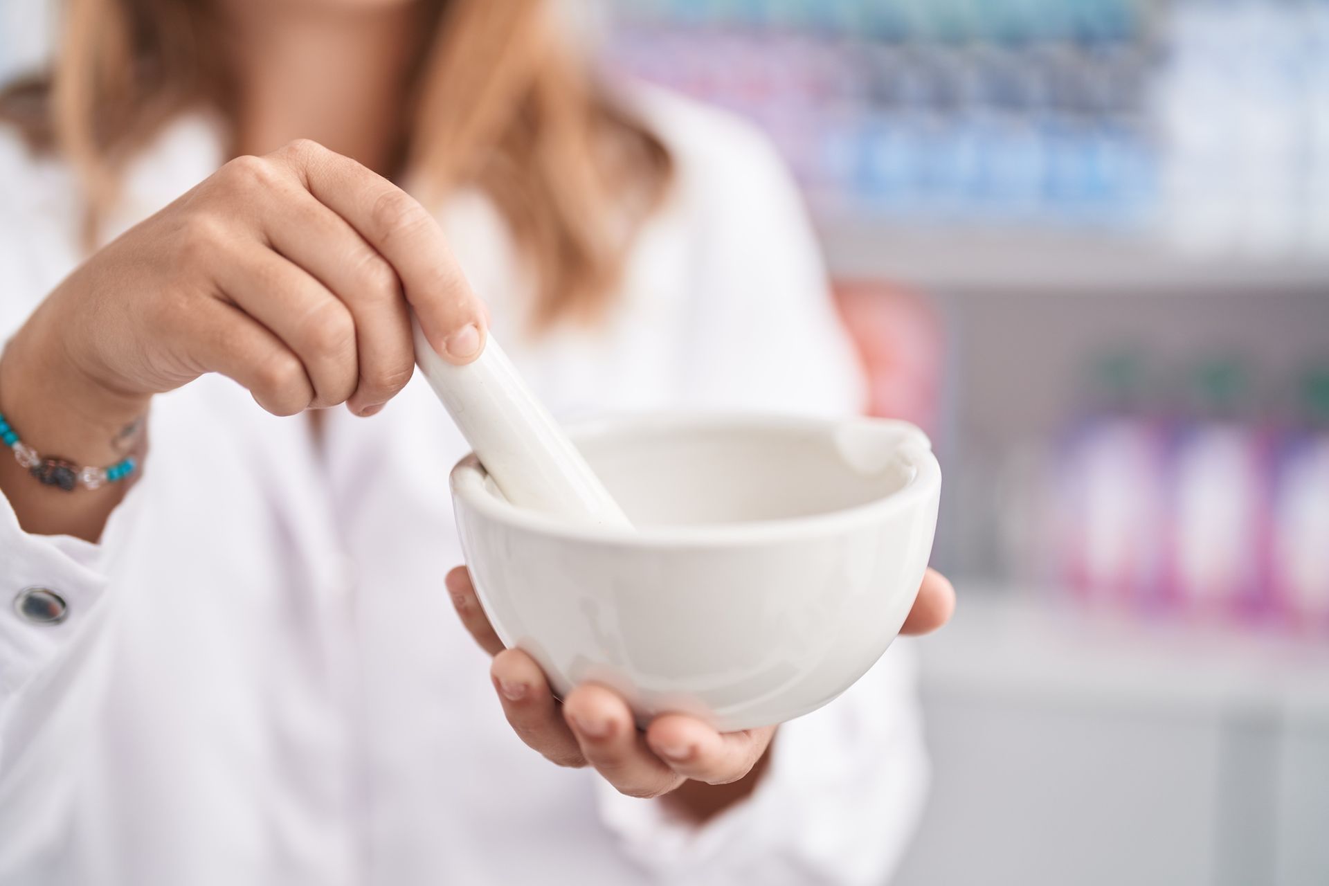 Una persona con un camice bianco utilizza un mortaio e un pestello in una farmacia.