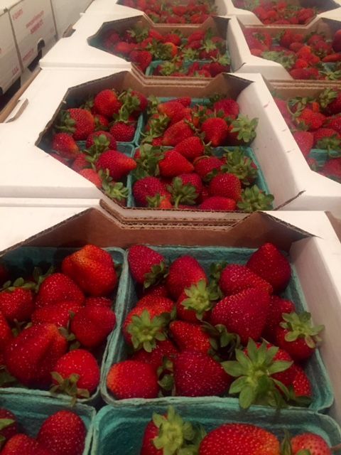 Fresh strawberries in green baskets inside cardboard containers.