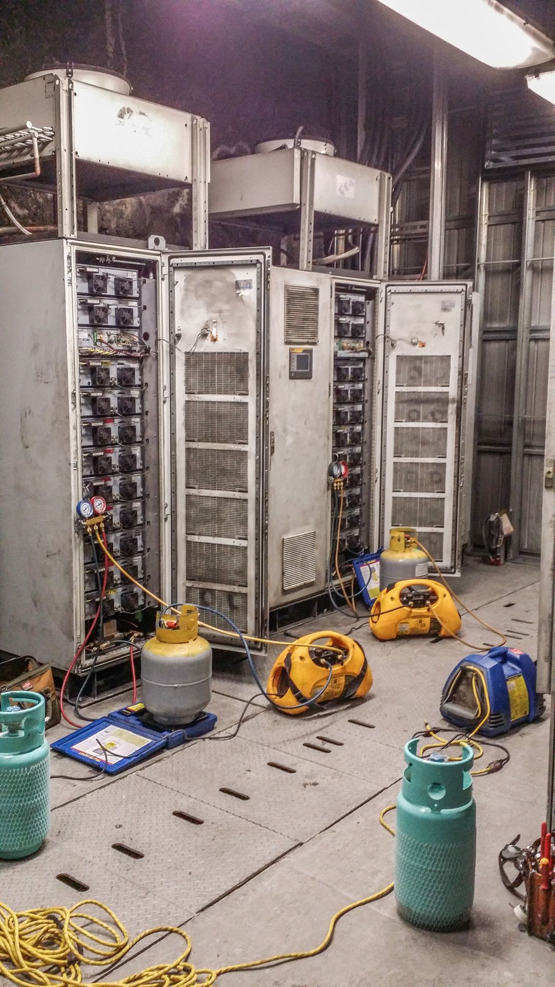 Machinery room with large metal cabinets, equipment, yellow tanks, and scattered tools.
