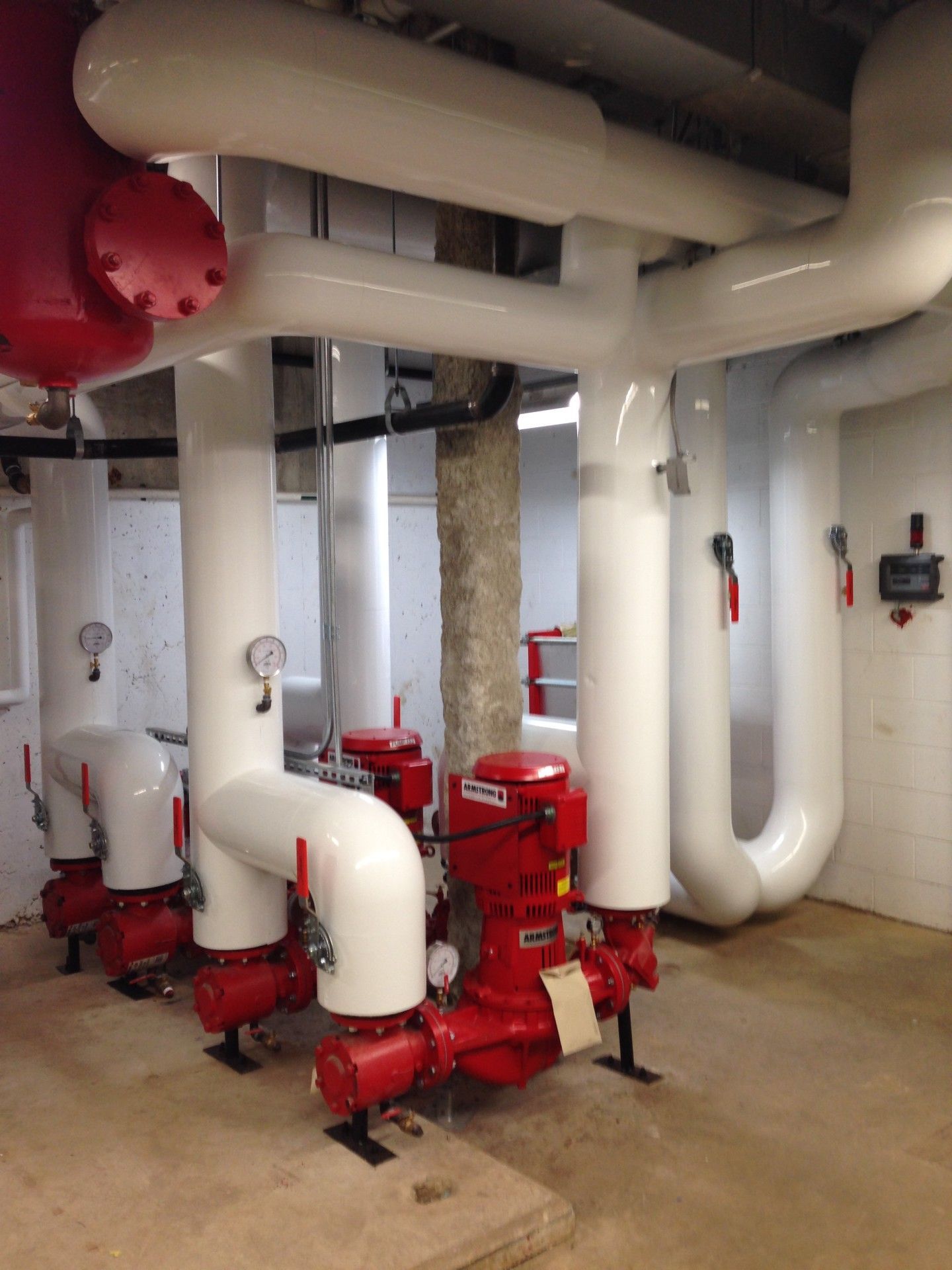 Red pumps with white insulated pipes in a mechanical room.