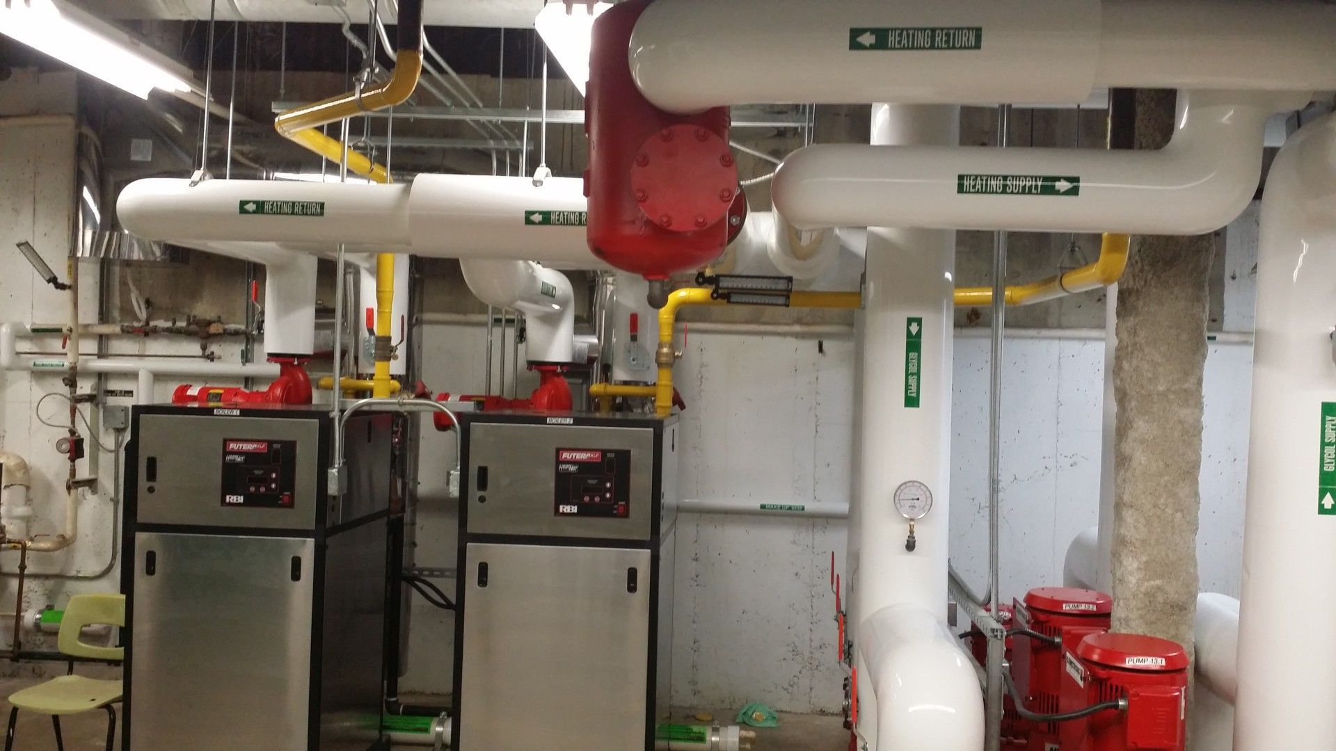 Mechanical room with white pipes, red components, and silver metal boxes.